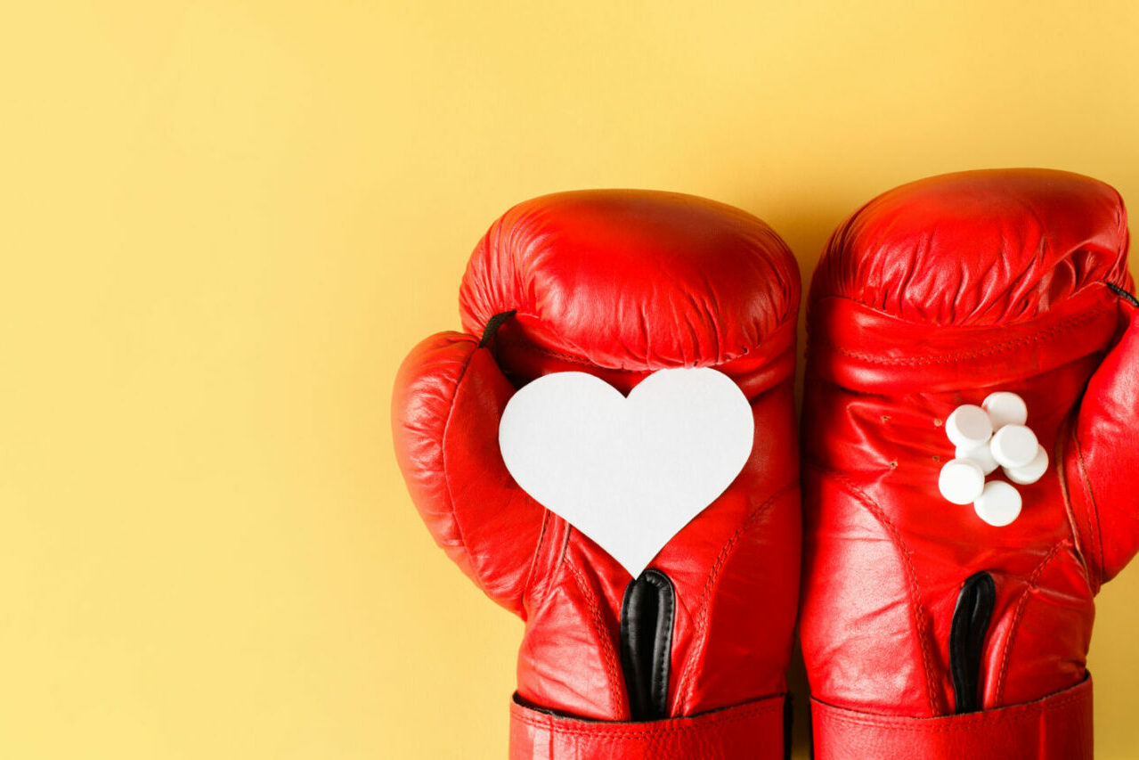 Rote Boxhandschuhe auf gelben Grund halten eine ausgeschnittenes Herz, das für Selbstliebe und Selfcare steht, und weiße Tabletten, die den neurobiologischen Aspekt der Hormone und Neurotransmitter symbolisieren.